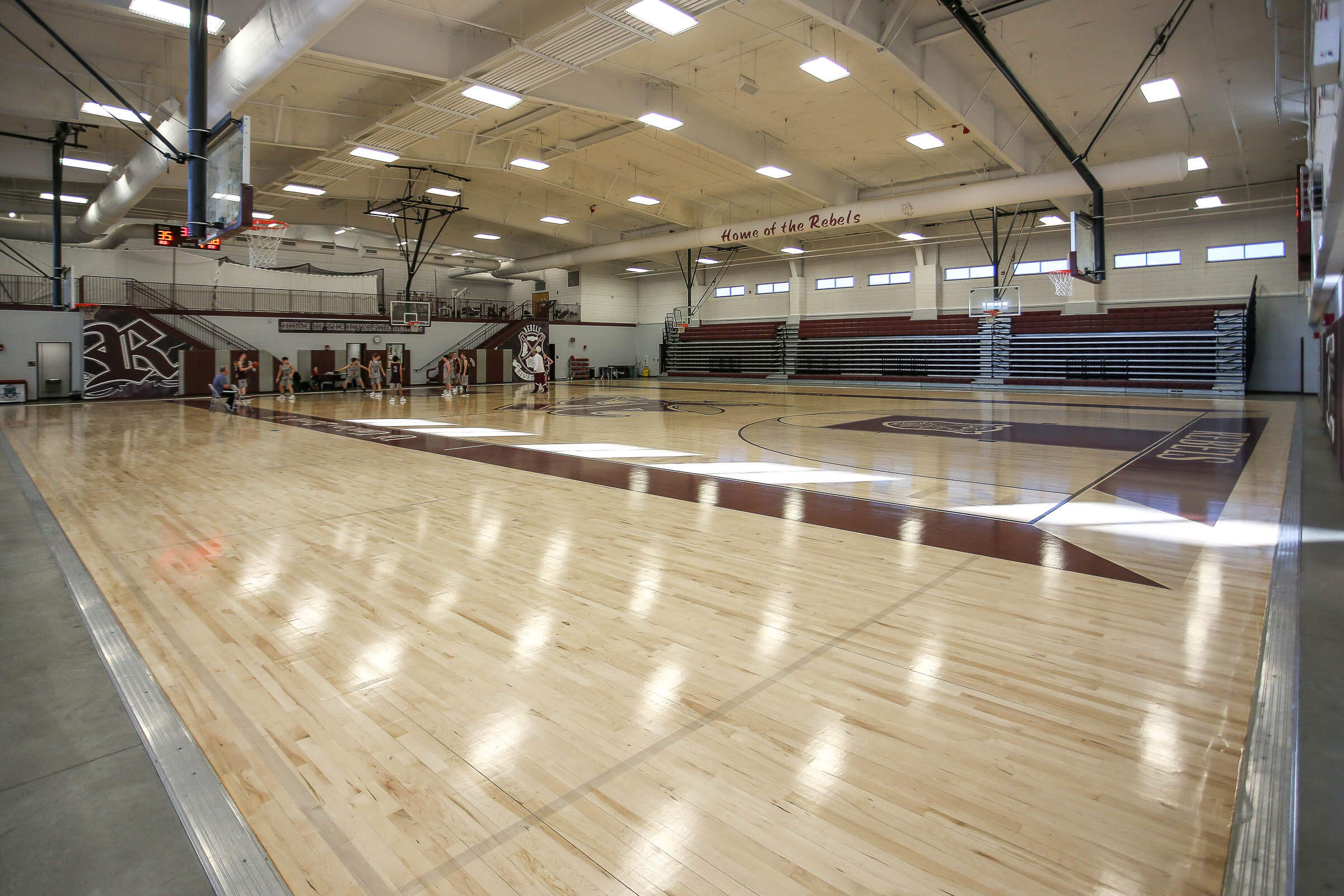 Wide gym view from the opposite side with polished floors and bleachers