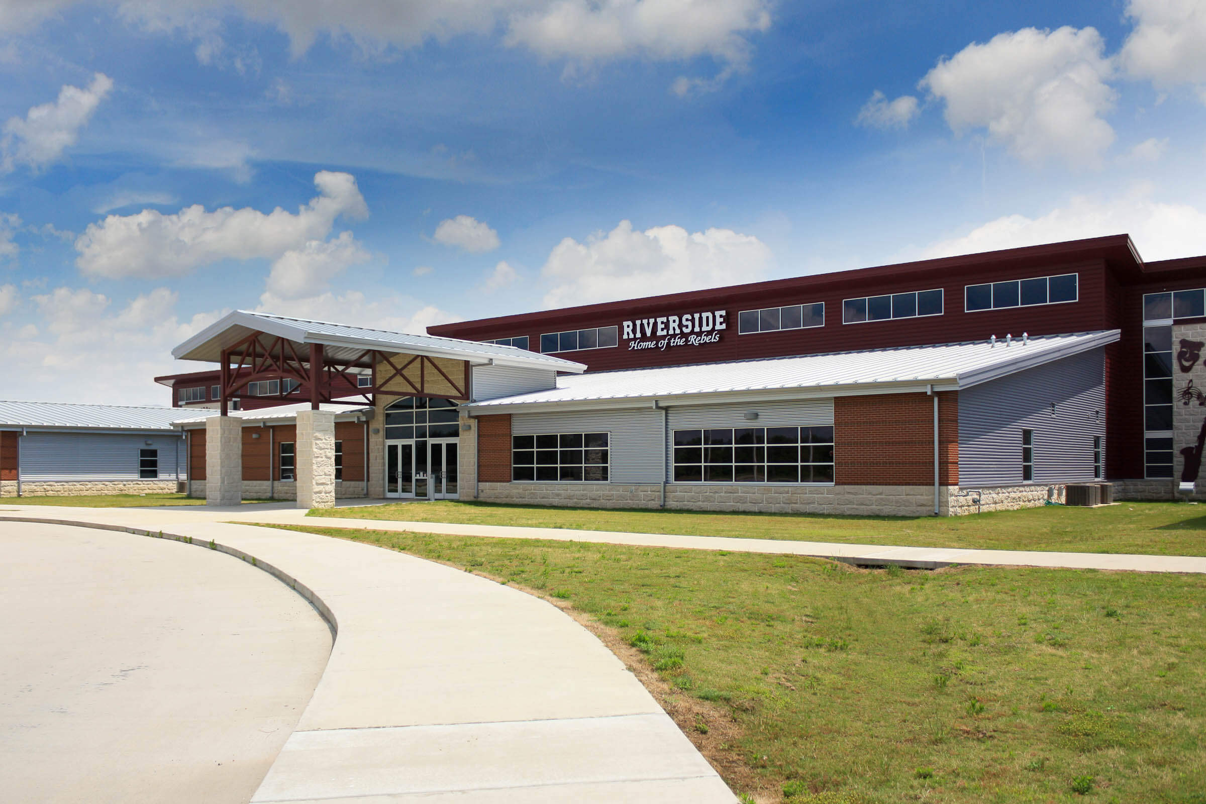 Front entrance with gabled canopy and “Riverside Home of the Rebels” sign flanked by large windows