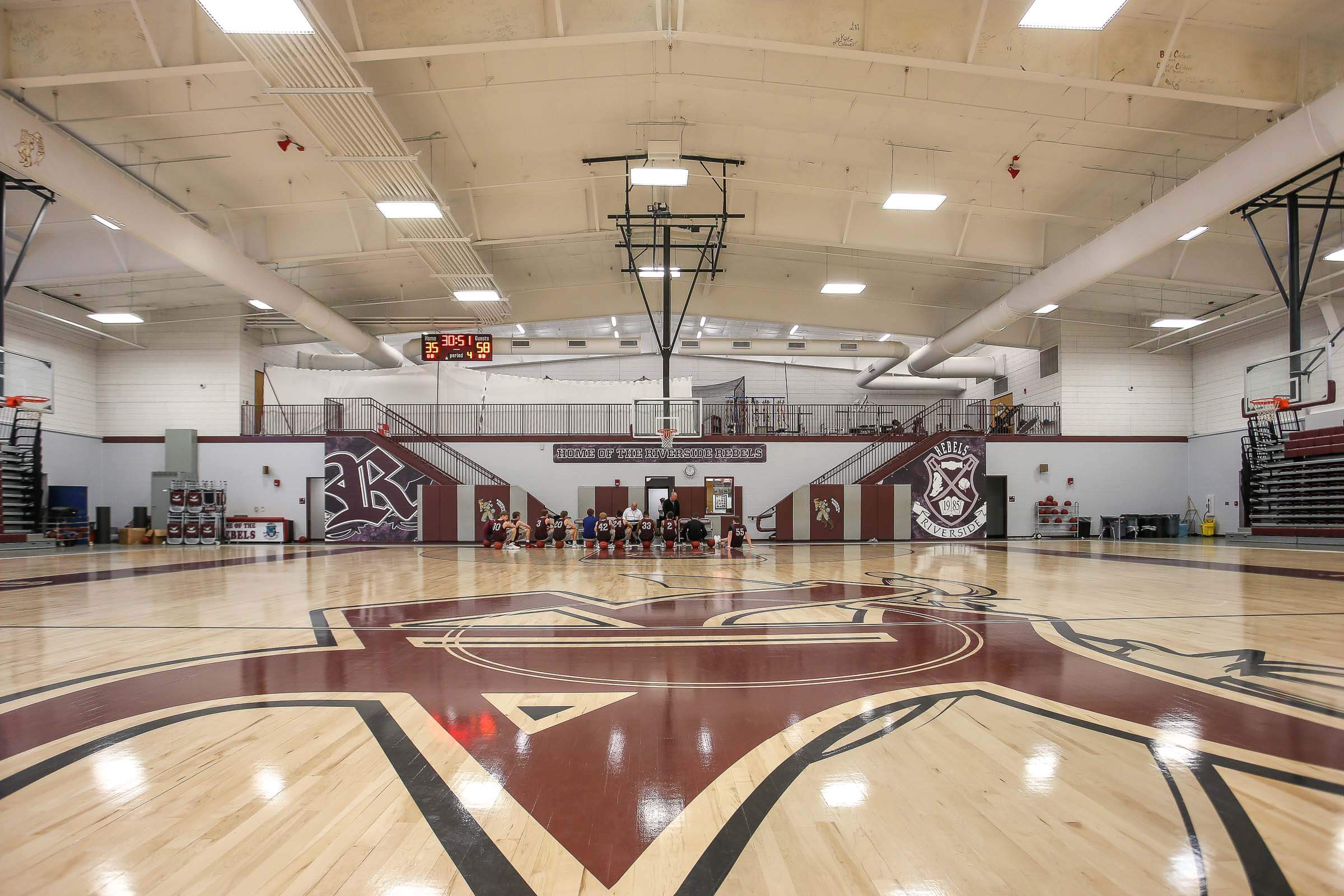 Interior of the gymnasium featuring polished maroon-and-white court, scoreboard, bleachers and center logo