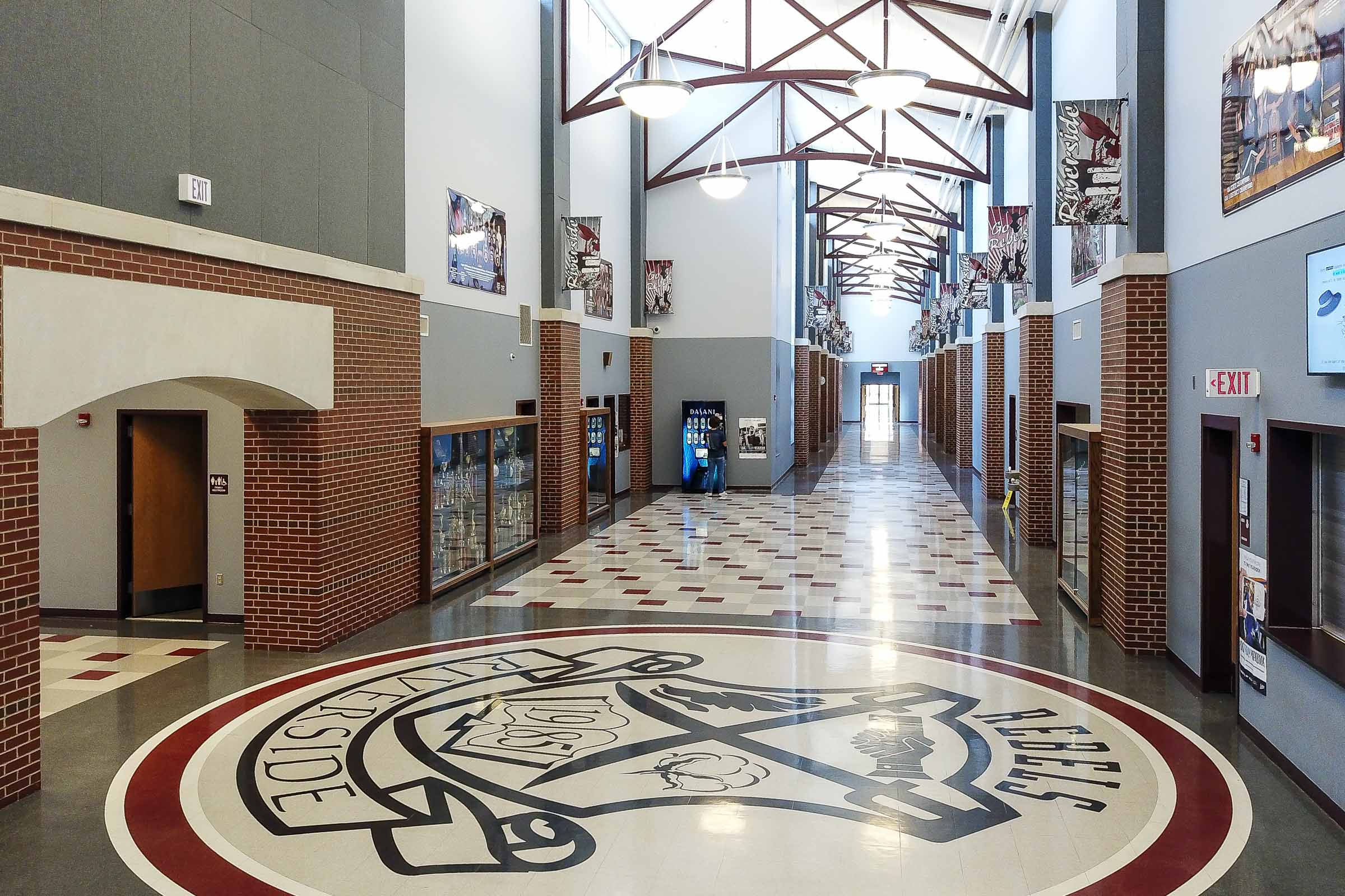 Corridor with high metal trusses, hanging banners and a large floor emblem near the entrance