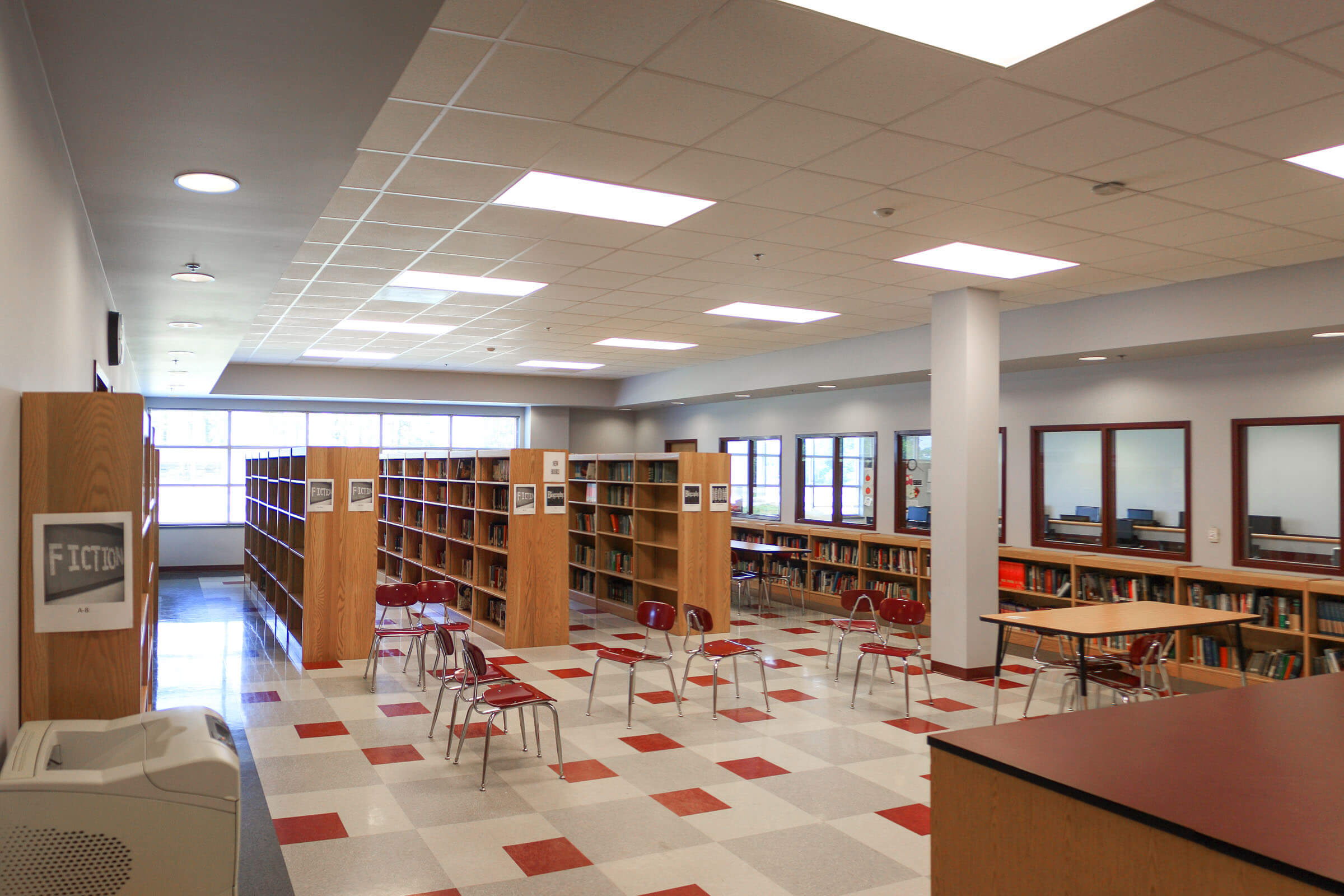 Library interior containing wooden shelves and tables arranged on a checkered floor