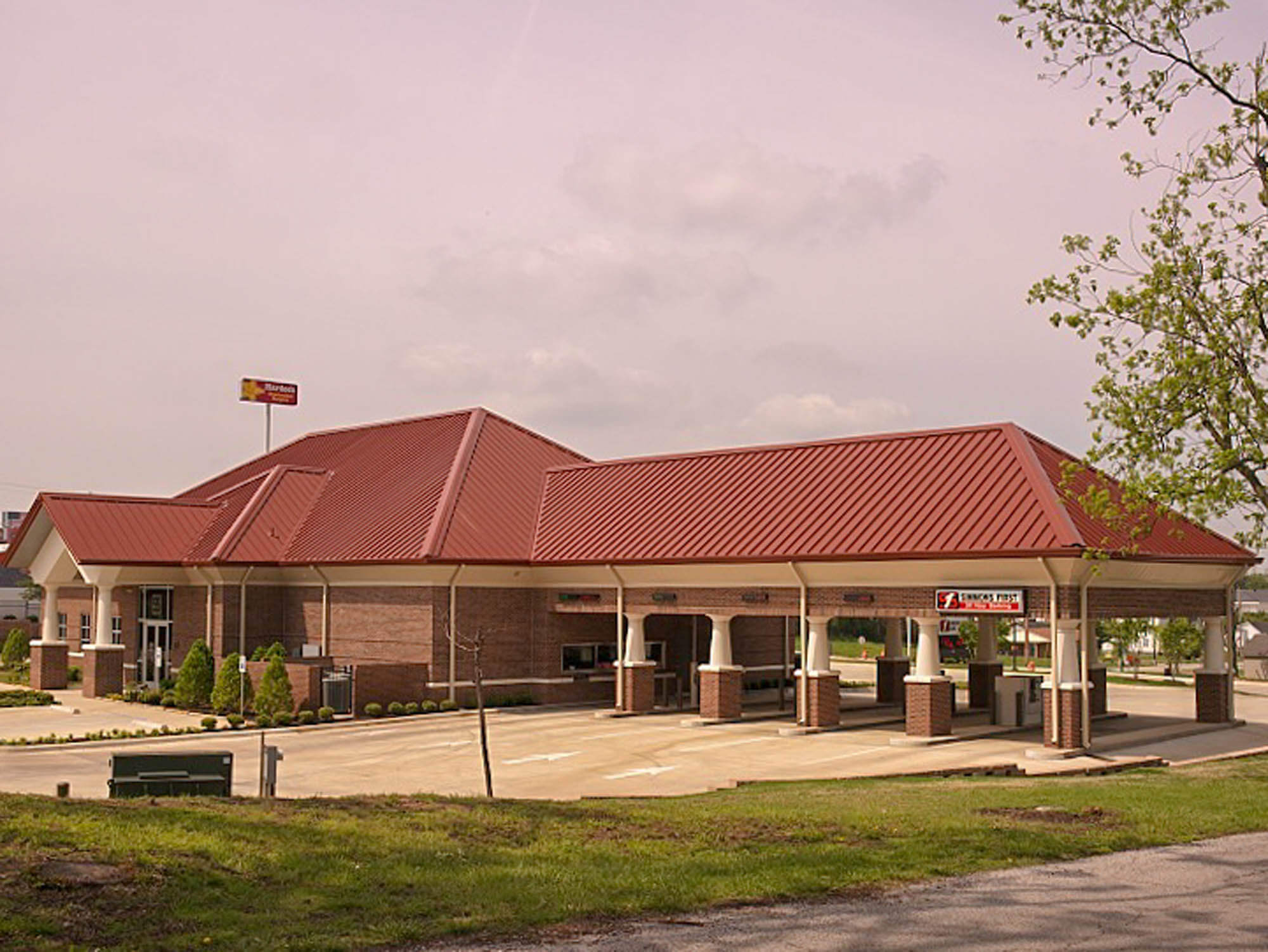 Angled view of the bank’s drive-through canopy featuring a red metal roof and brick columns with the main building behind
