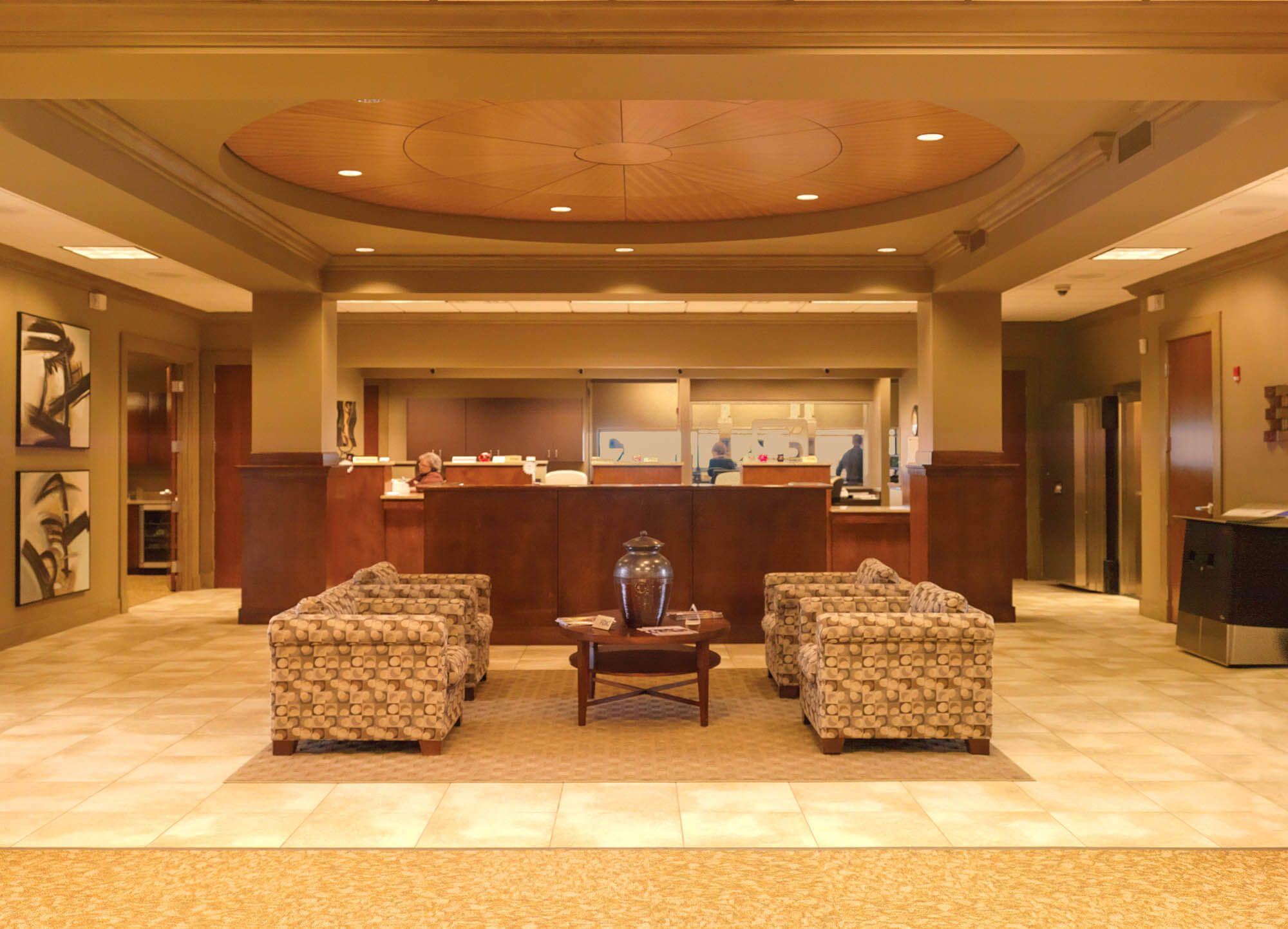 Lobby interior with patterned armchairs surrounding a coffee table, wood ceiling accent and teller counter in the background