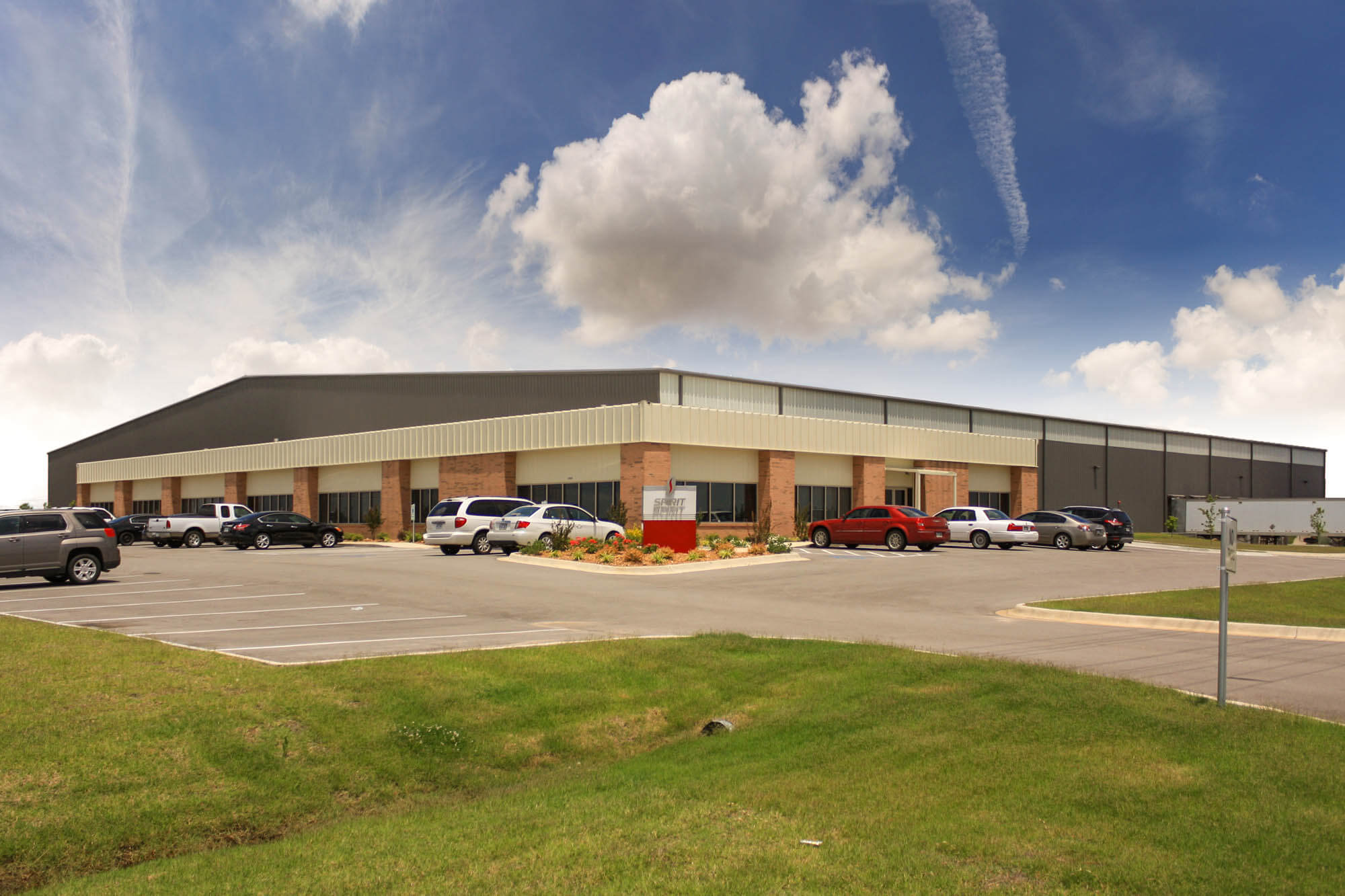 Oblique exterior shot of the facility with dark-grey warehouse section attached to a lighter office wing and cars in the parking lot