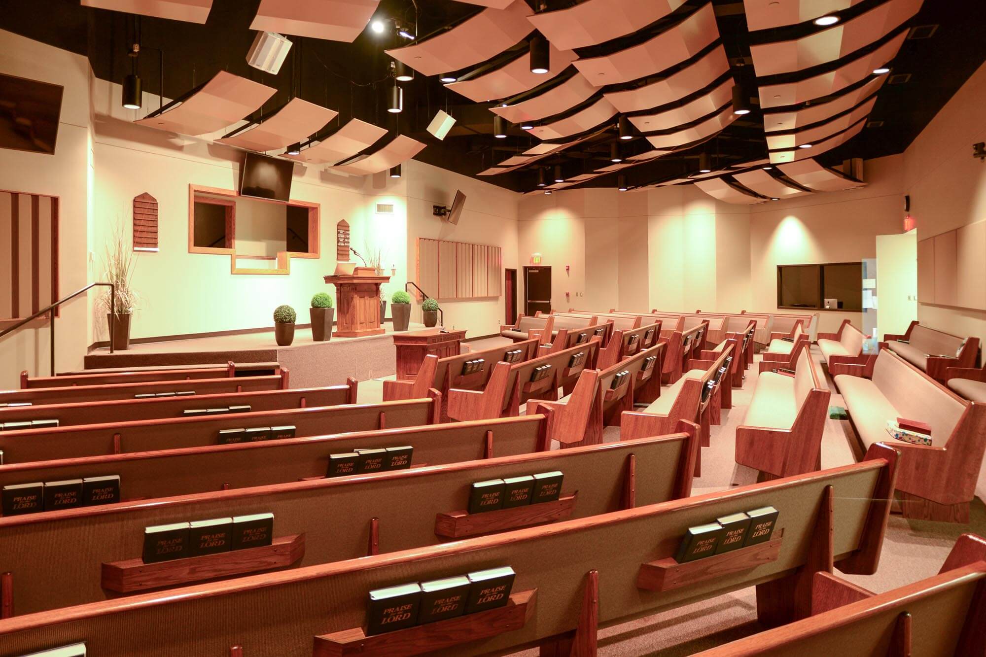Interior of Stoneridge Church of Christ auditorium with wooden pews, stage, and acoustic ceiling panels
