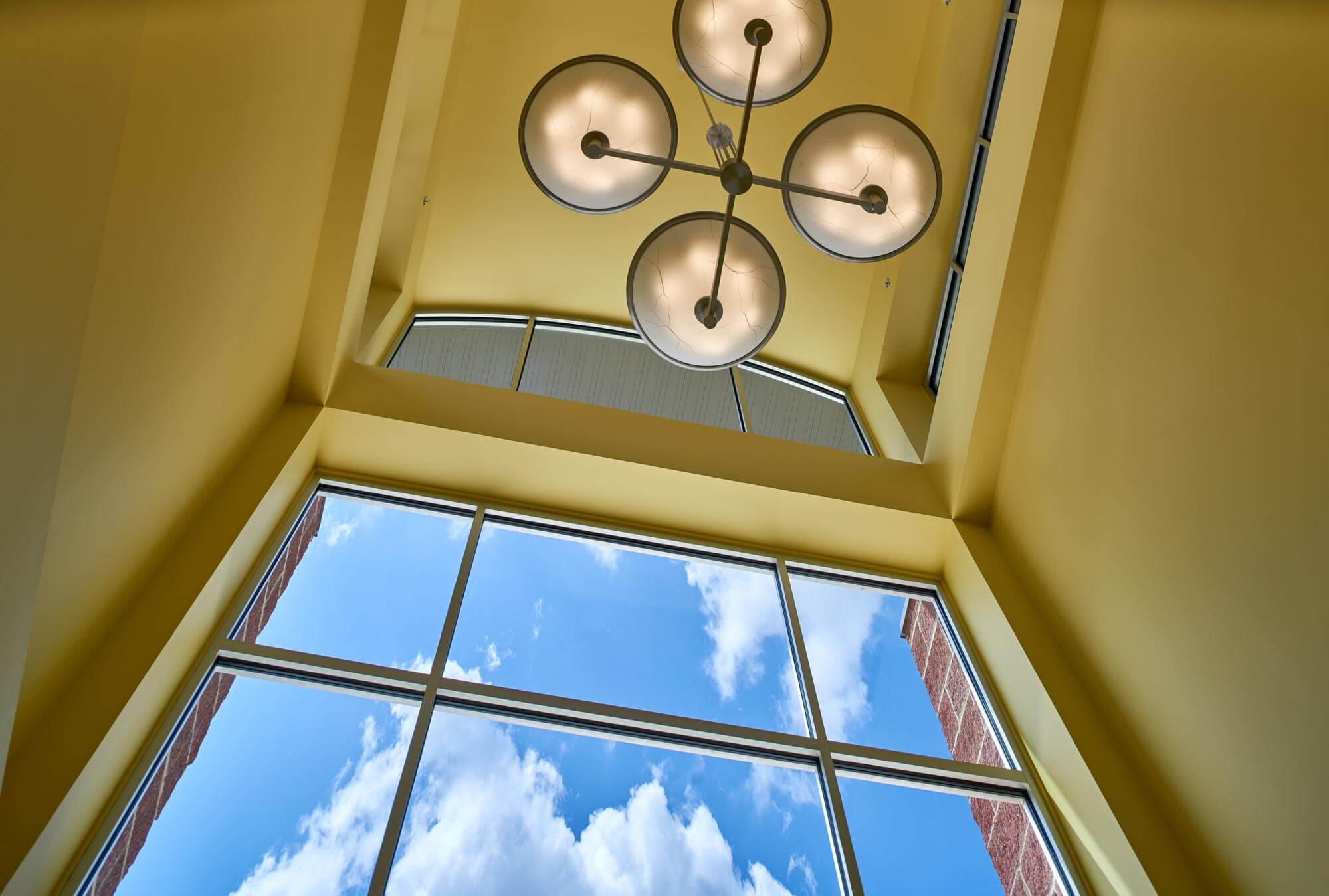 Interior view of Trumann Elementary entryway ceiling with modern chandelier and tall windows showing blue sky