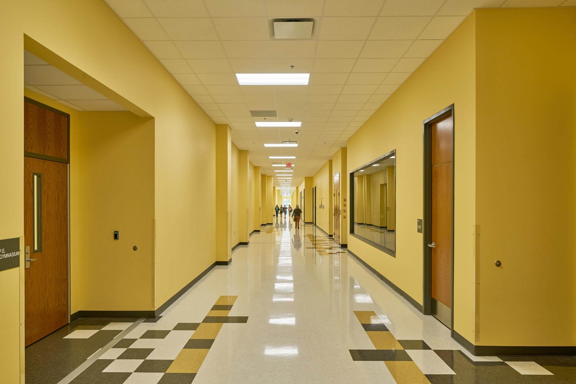 School hallway interior with yellow walls, patterned tile floor, and students walking in the distance