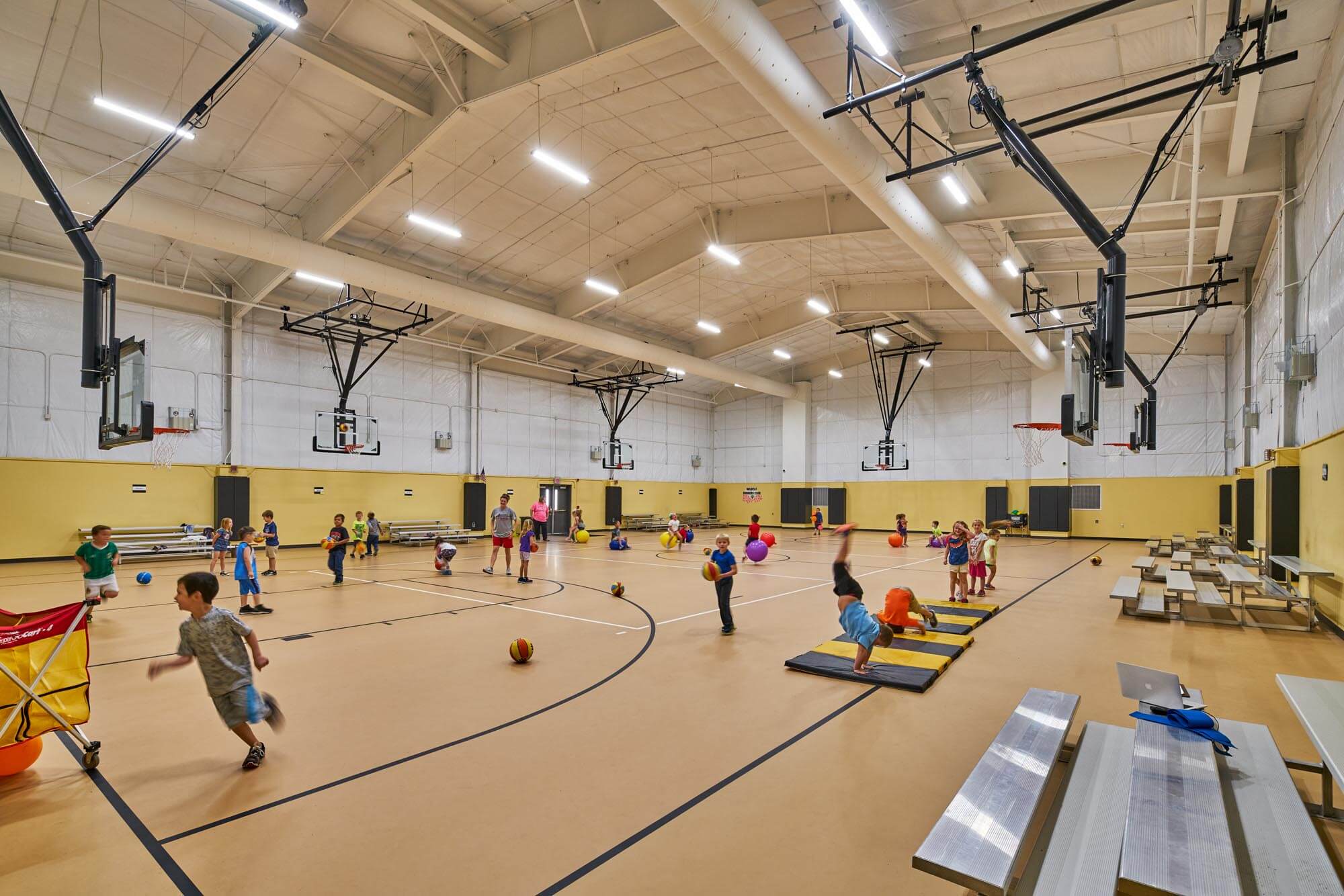 School gymnasium with children playing, basketball hoops, and bleachers