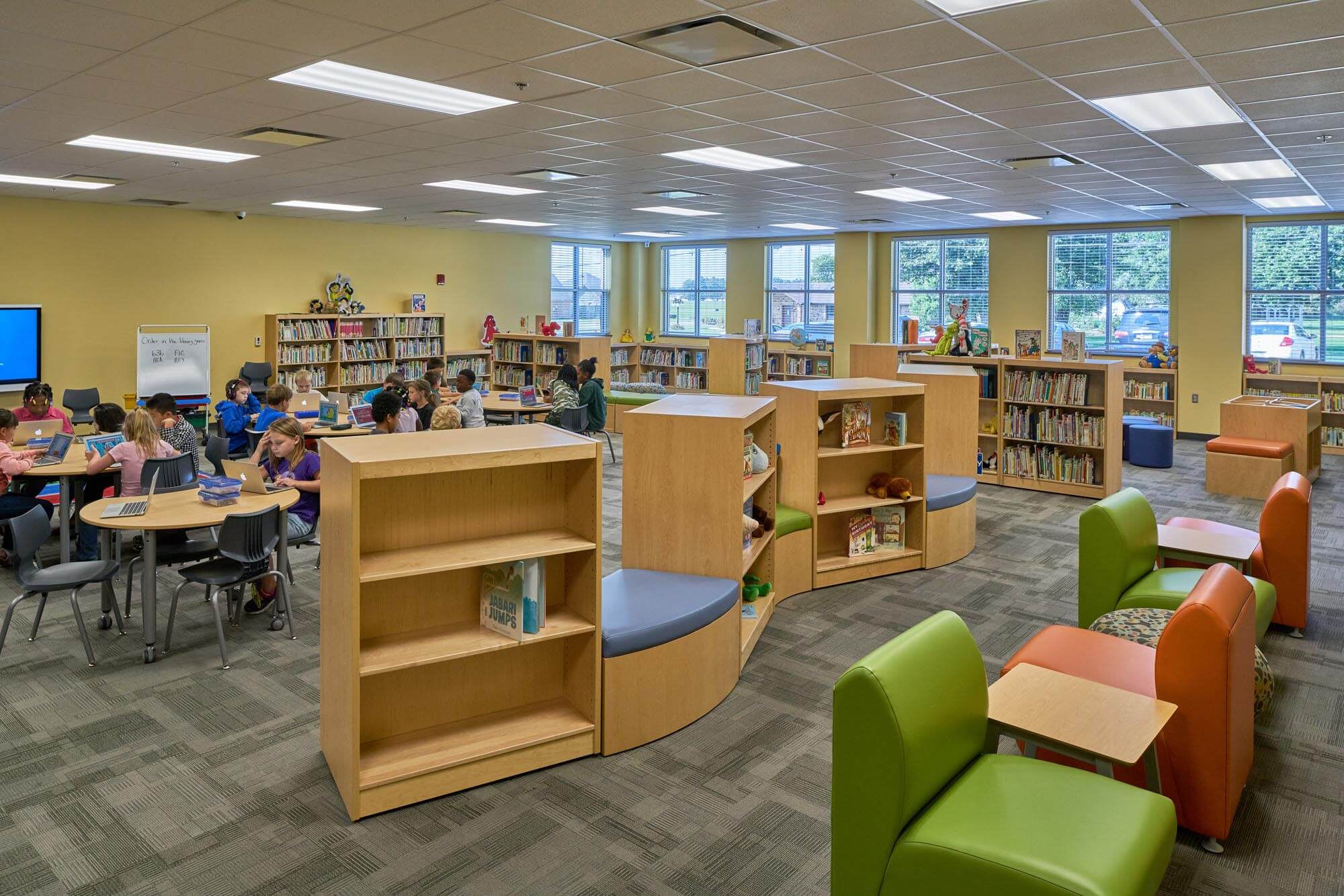 Elementary students using laptops at round tables in a school library