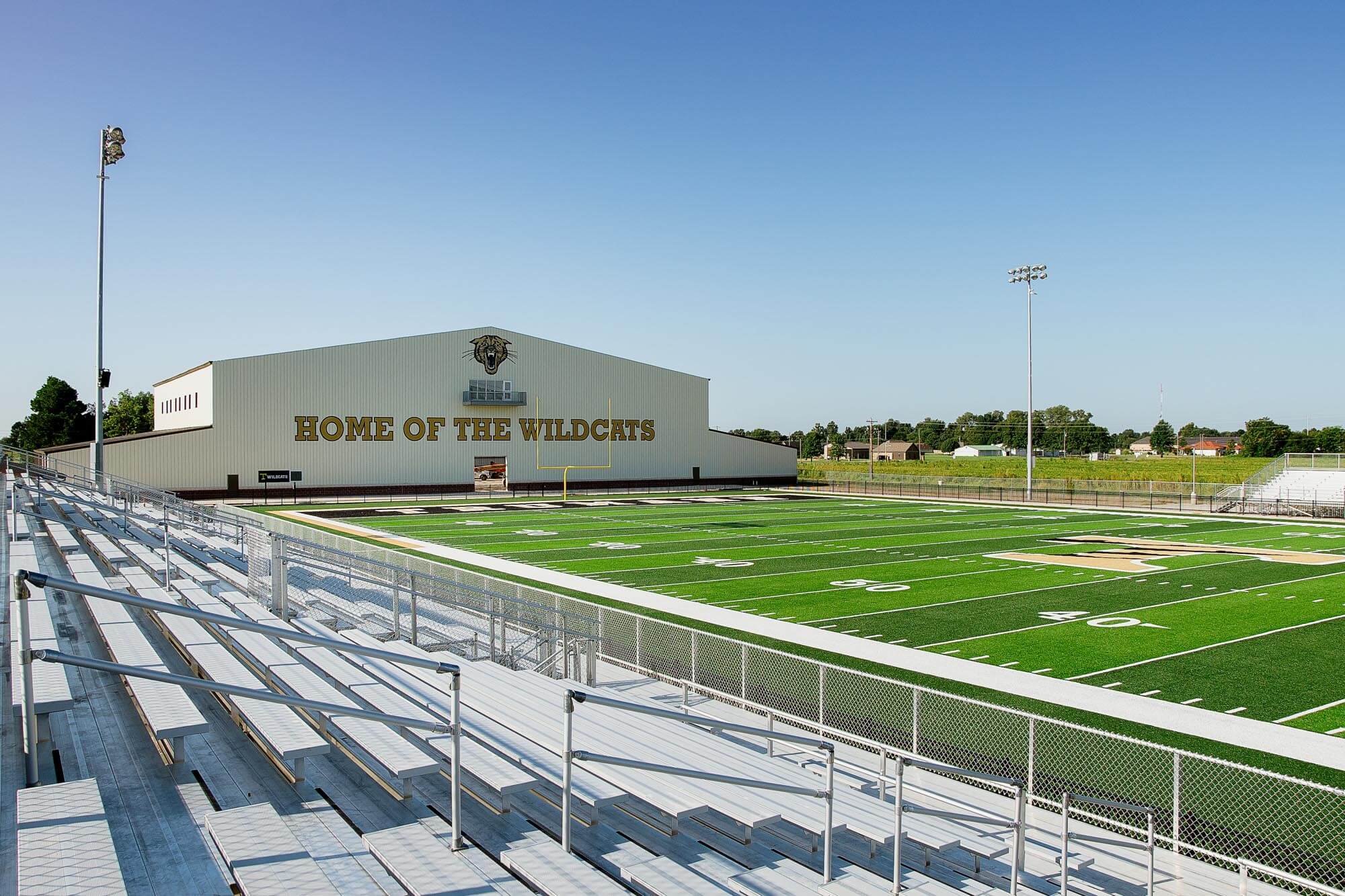 Field view from the stands highlighting the fieldhouse and 'Home of the Wildcats' banner in the background
