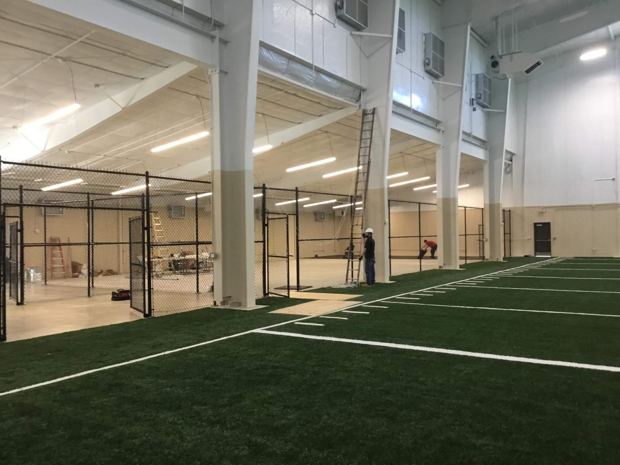 Interior of the indoor practice facility under construction with artificial turf and chain-link netting