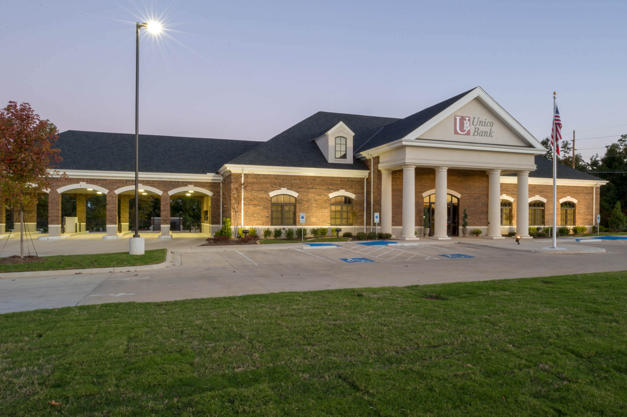 Front exterior view at dusk showing brick walls, gabled roofs, accessible parking and drive-through lanes set against a lawn