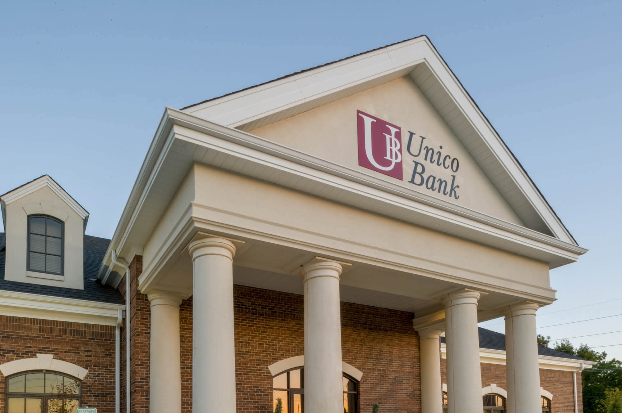 Close-up of the pediment over the main entrance with the Unico Bank logo, flanking columns and lanterns