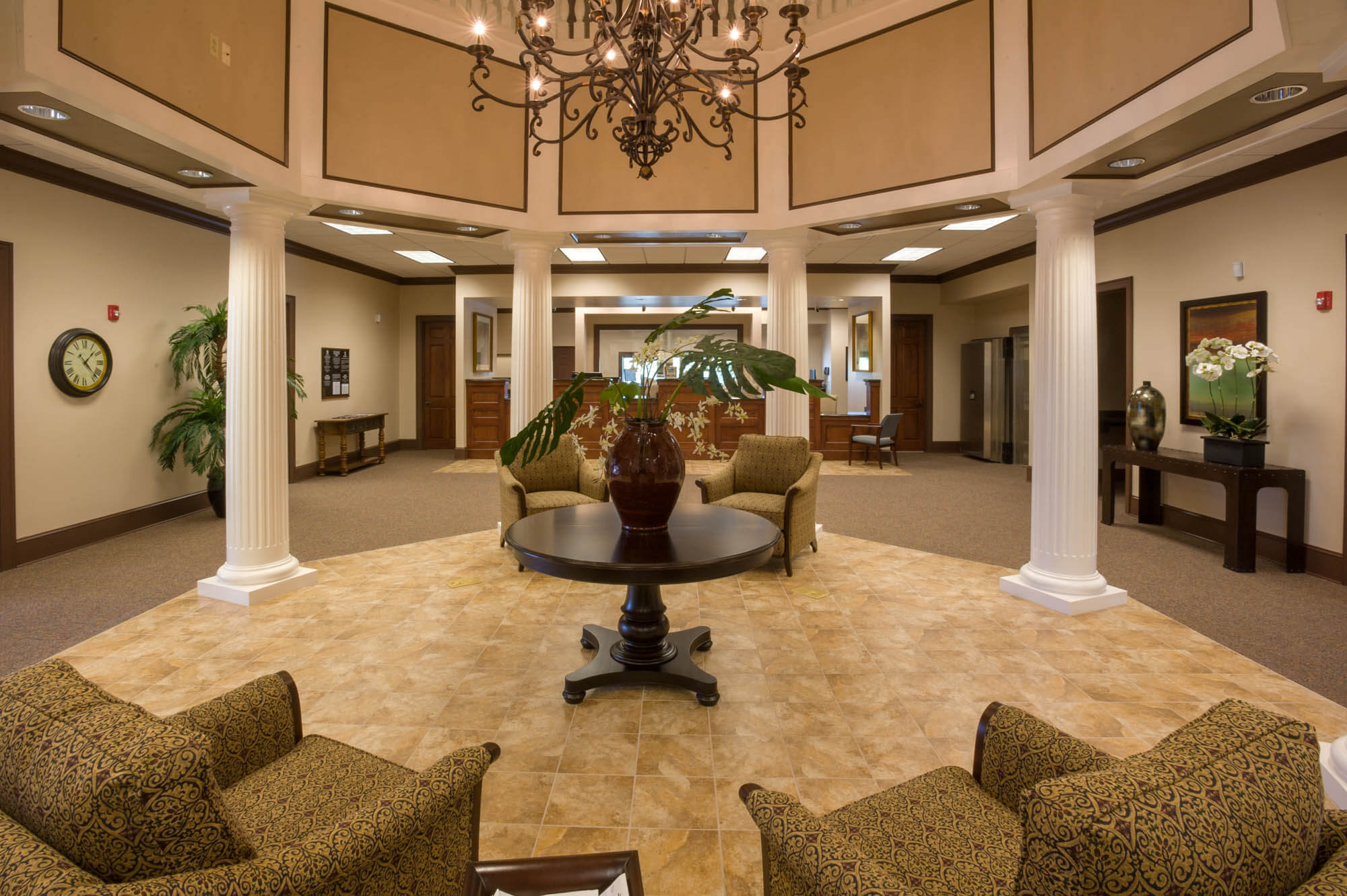 Interior lobby with chandelier, white columns, seating area and tile floor transitioning to carpet