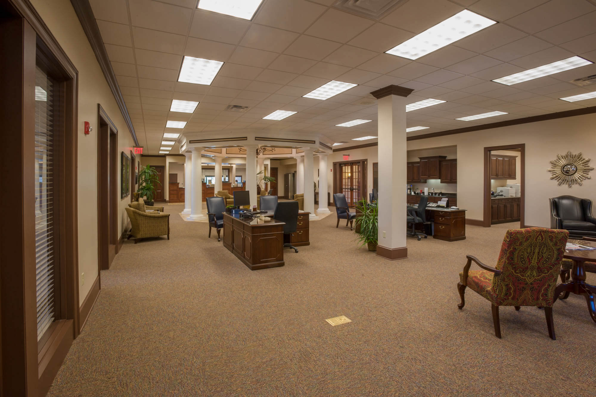 Open-plan office interior featuring desks, potted plants and white columns beneath a high ceiling
