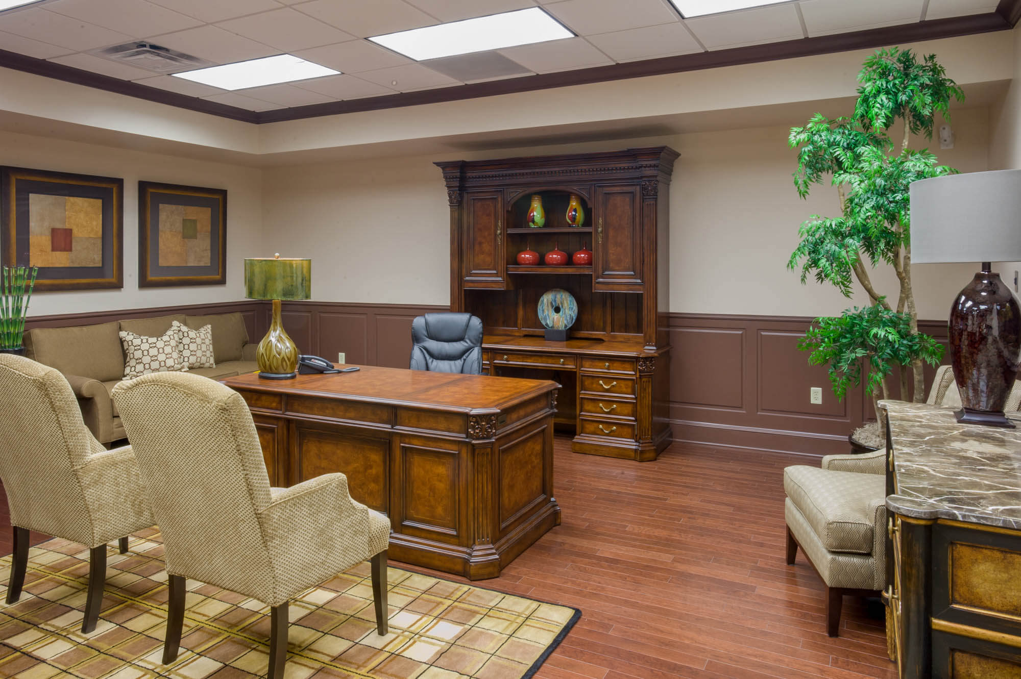 Executive office with wooden desk, matching hutch, visitor chairs and a large potted plant