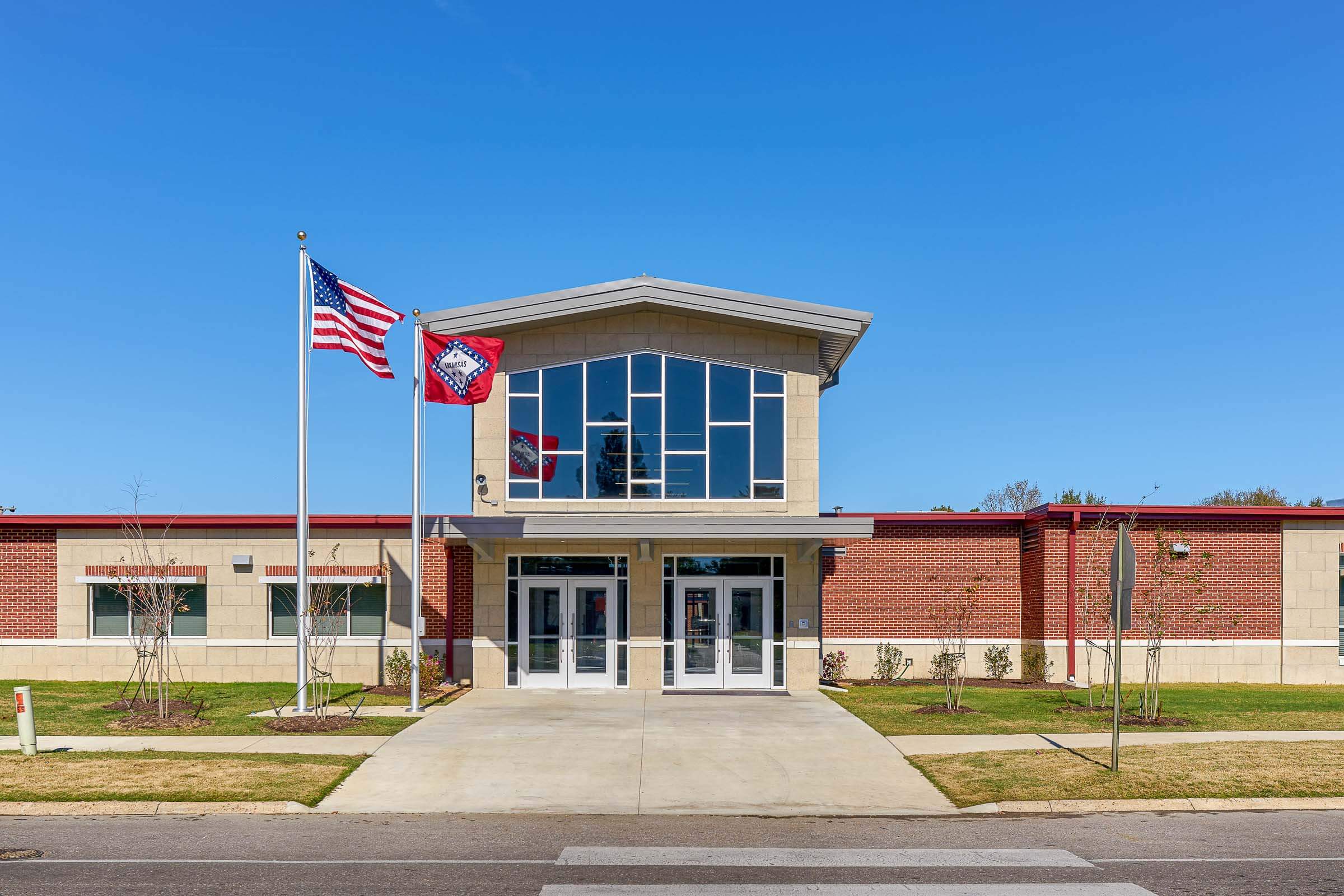 Front entrance of the school with glass façade, sloped roof and U.S. and Arkansas flags flying on flagpoles