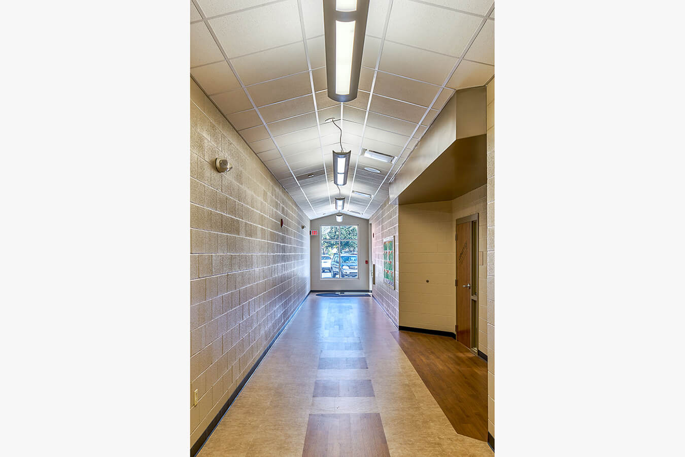 Narrow corridor with cinder-block walls and drop ceiling leading to an exit door